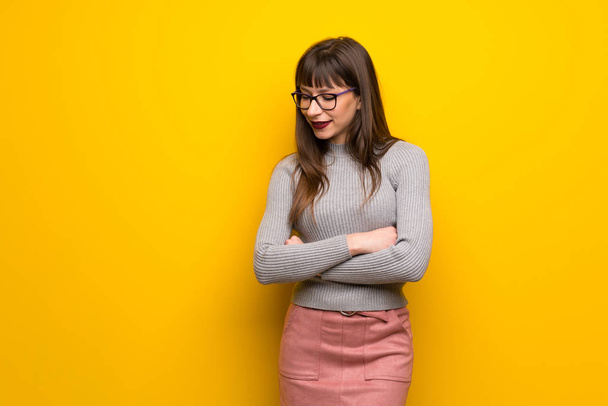 Femme avec des lunettes sur le mur jaune regardant vers le bas avec la main sur le menton
 - Photo, image