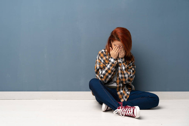 Young redhead woman sitting on floor with tired and sick expression - Foto, afbeelding