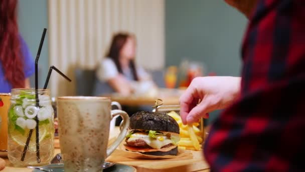 Una pareja sentada a la mesa en un café y camarero trae el orden. Dos hamburguesas negras
 - Metraje, vídeo