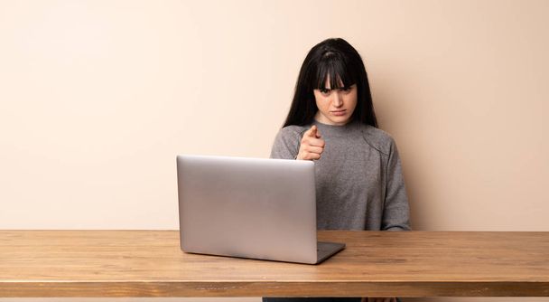 Mujer joven trabajando con su portátil frustrado y señalando hacia el frente
 - Foto, imagen
