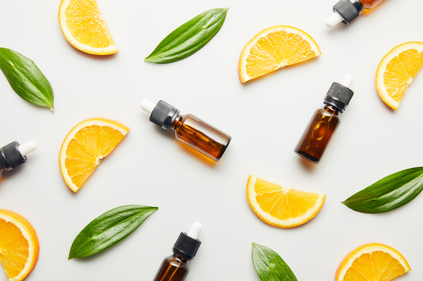 Flat lay with essential oil bottles, orange slices and green leaves on white background - Foto, afbeelding