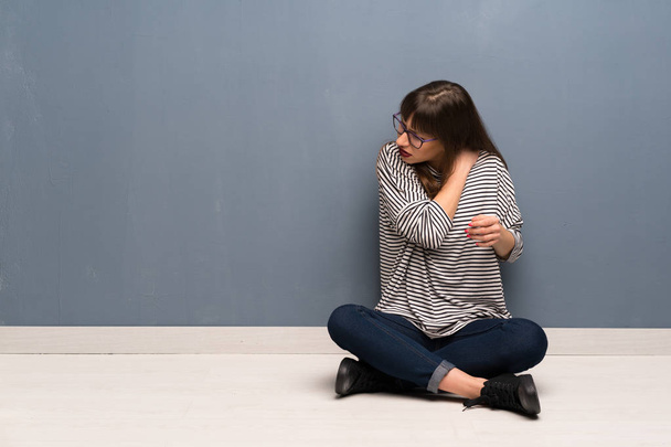 Γυναίκα με τα γυαλιά, κάθεται στο πάτωμα που πάσχουν από τον πόνο στον ώμο για να κάνει μια προσπάθεια - Φωτογραφία, εικόνα