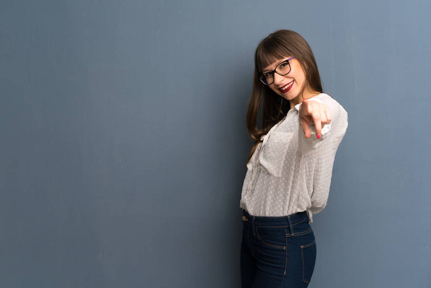 Femme avec des lunettes sur le mur bleu pointe du doigt vers vous avec une expression confiante
 - Photo, image