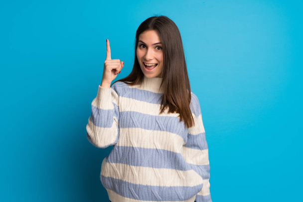Młoda kobieta nad niebieską ścianą zamierzający realizuje rozwiązanie podczas podnoszenia palca - Zdjęcie, obraz