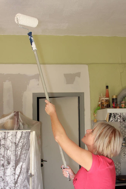 Mujer rubia joven pintando el techo interior de una habitación
 - Foto, imagen