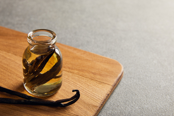 Vanilkové lusky a esenciální olej na dřevěné krájecí desky na tmavý podklad - Fotografie, Obrázek