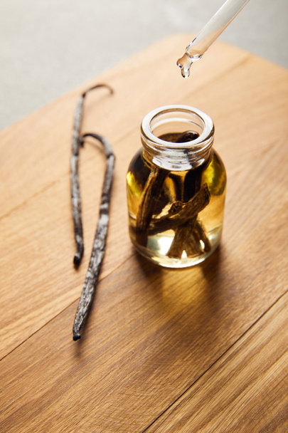 Glass bottle of essential oil with vanilla pods on wooden cutting board - Photo, Image