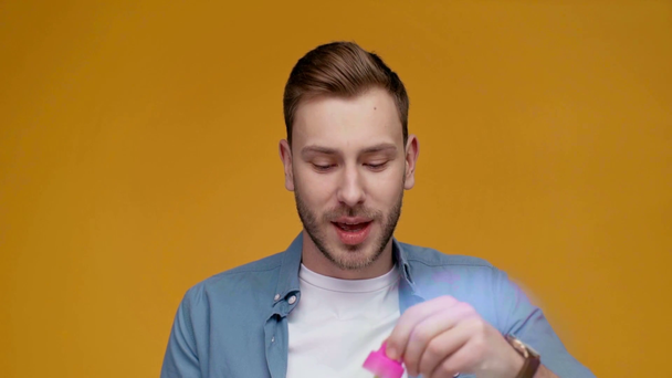 handsome man blowing soap bubbles, smiling and looking at camera in slow motion isolated on yellow - Footage, Video