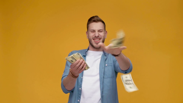 handsome excited man throwing dollar banknotes and smiling in slow motion isolated on yellow - Séquence, vidéo