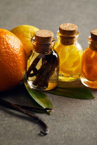Bottles of essential oil with lemon, orange and vanilla on dark surface - Foto, Bild