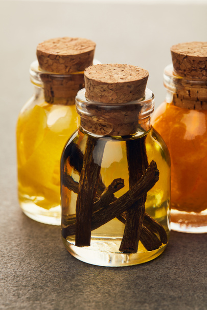 Glass bottles of essential oil with vanilla and cut fruits on dark surface - Photo, Image