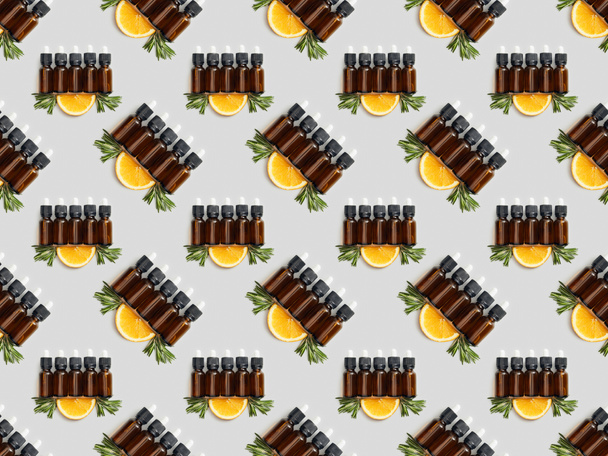 Μοτίβο με καφετιά μπουκάλια με αιθέριο έλαιο και φέτες πορτοκάλι σε γκρίζο φόντο - Φωτογραφία, εικόνα