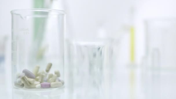 Panning view of pill dropping to glass container - Πλάνα, βίντεο