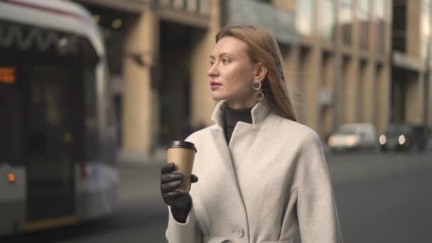 Attractive woman holding a cup of coffee waiting for the taxi - Video