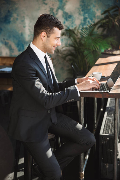 Bello giovane uomo d'affari in abiti formali all'interno in caffè utilizzando il computer portatile
. - Foto, immagini