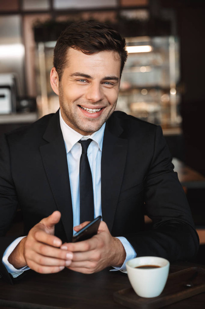 Handsome young businessman in formal clothes indoors in cafe using mobile phone. - Foto, afbeelding