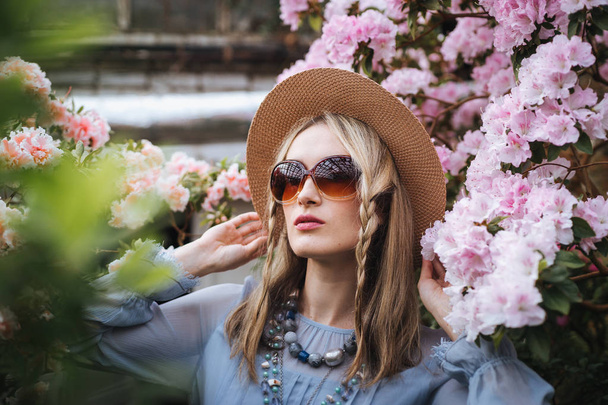 blonde woman in hat and glasses posing on colorful flowers background  - Photo, image