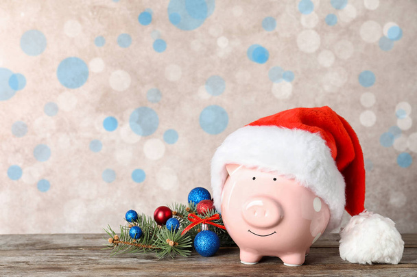 Cute piggy bank with Santa hat on table, space for text. Bokeh effect - Foto, imagen