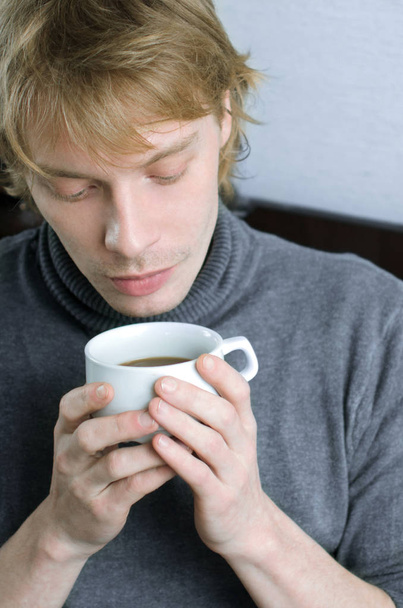 mladý muž v šedém svetru s šálkem kávy v ruce - Fotografie, Obrázek