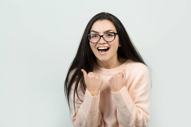 Happy young caucasian female in a pink jumper. Emotional portrait of a girl with gesturing action on a gray background. Conceptual business stub. - Foto, imagen