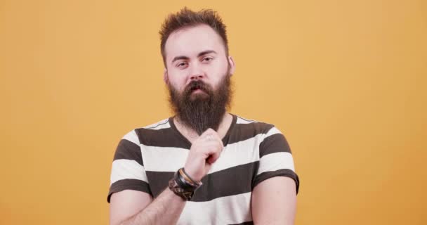 Pretty young bearded man dressed in a t-shirt in front of yellow background - Footage, Video