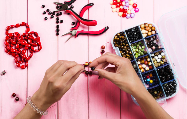 Jewelry making. Female hands with a tool on a pink background.  - Photo, Image