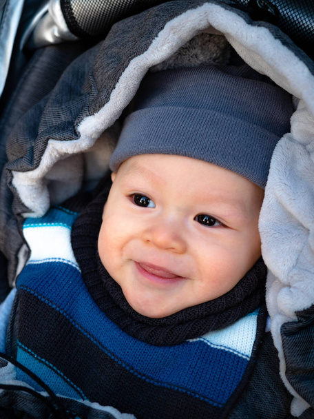 Ritratto ravvicinato di dolce neonato avvolto nella busta invernale all'aperto, felice bambino ridente che si gode una passeggiata in un parco invernale innevato seduto in un passeggino caldo con cappuccio di pecora
. - Foto, immagini