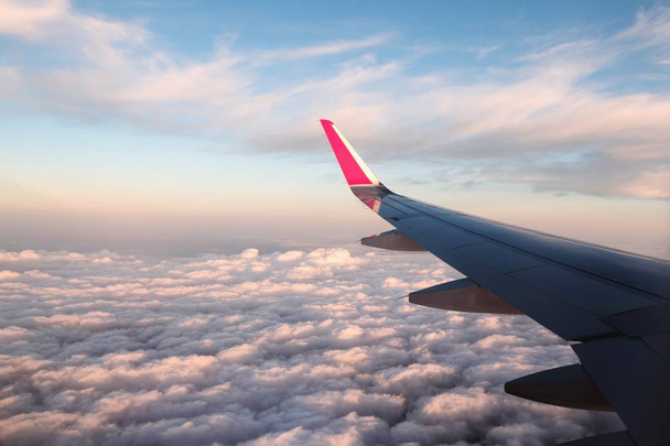 Vliegtuigvleugel op een vlucht boven de wolken tijdens de zonsondergang - Foto, afbeelding