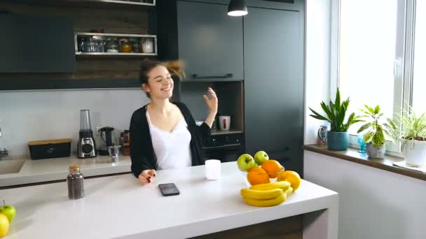 Smiling woman unbinding her hair. Drinking coffee and looking at the smartphone. Home, at the kitchen. - Video, Çekim