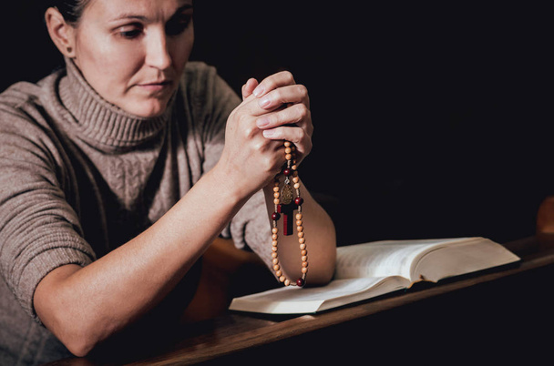 Christian woman praying in church. Hands crossed and Holy Bible on wooden desk. Background - Фото, зображення
