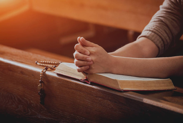 Christian woman praying in church. Hands crossed and Holy Bible on wooden desk. Background - Foto, Bild