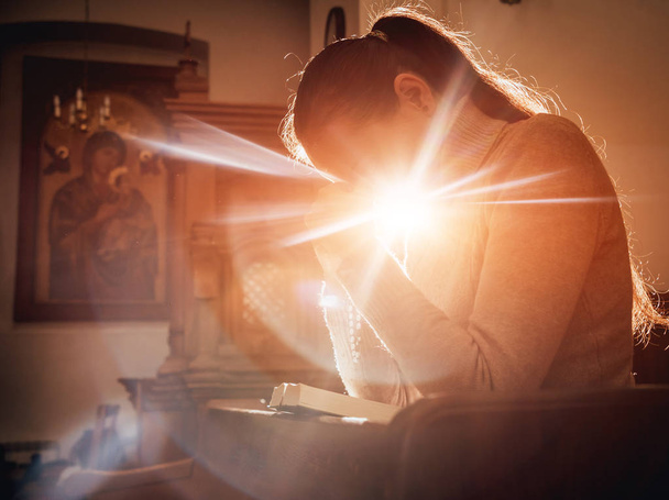 Kristitty nainen rukoilee kirkossa. Kädet ristiin ja Raamattu puupöydälle. Taustaa
 - Valokuva, kuva