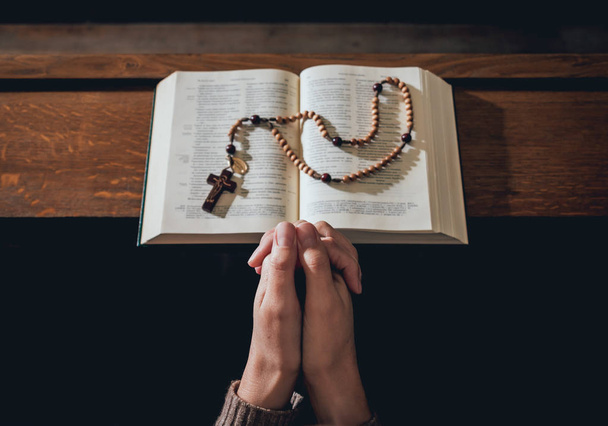 Christian woman praying in church. Hands crossed and Holy Bible on wooden desk. Background - Foto, immagini