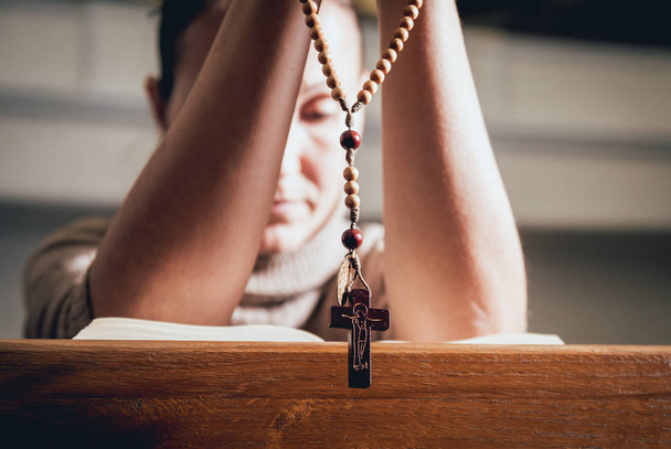 Christian woman praying in church. Hands crossed and Holy Bible on wooden desk. Background - Foto, immagini