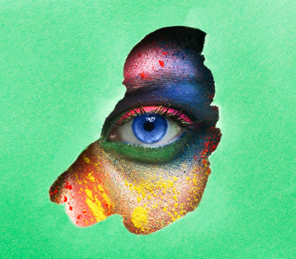 helles weibliches Auge, das durch ein Loch in Papier blickt - Foto, Bild