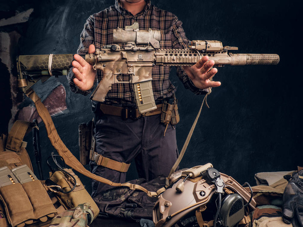 Mann im karierten Hemd hält Sturmgewehr in der Hand und zeigt seine Militäruniform und Ausrüstung. moderne Ausrüstung für Spezialeinheiten. - Foto, Bild