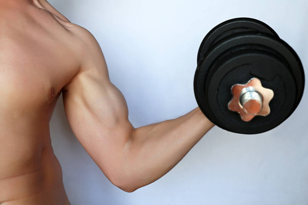 Athletic guy training with dumbbell, exercises for biceps. Concept of weightlifting in the gym, bodybuilding - Photo, Image
