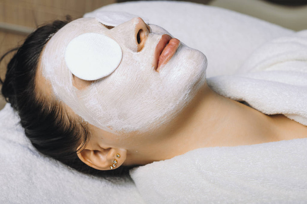 Close up de uma mulher caucasiana esperando com os olhos fechados com uma máscara anti idade hialurônica em seu rosto fazendo um tratamento facial em um centro de spa
. - Foto, Imagem
