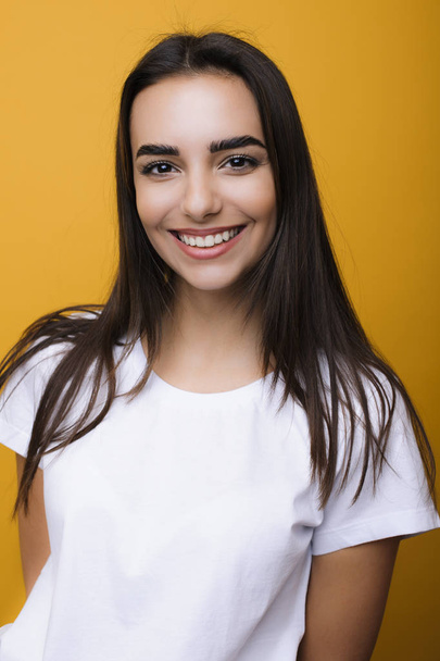 Porträt einer schönen kaukasischen Frau in weißem Hemd, die vor einer gelben Wand lachend in die Kamera blickt. - Foto, Bild