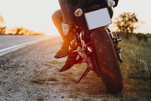 Вид на урожай ног мотоциклиста, сидящего на велосипеде во время путешествия по миру против заката
. - Фото, изображение