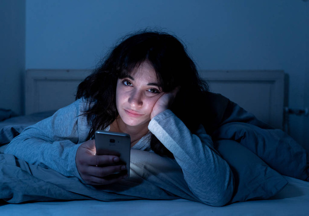 Attractive latin woman addicted to mobile phone and internet late at nigh in bed looking sleepless - Photo, image