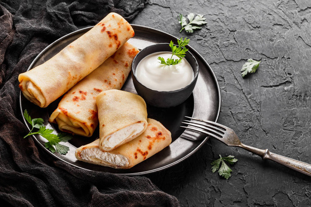 Crepes with cottage cheese, greens and sour cream on black plate over dark background. Pancake week or Shrovetide. Healthy breakfast. Top view, flat lay - Φωτογραφία, εικόνα