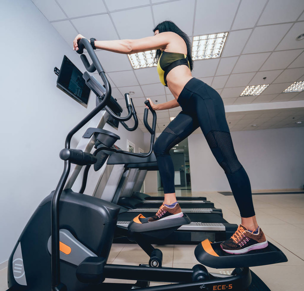 Young woman training on cross trainer at the gym. Peoples in fitness center. Treadmill. Health concept - Fotó, kép
