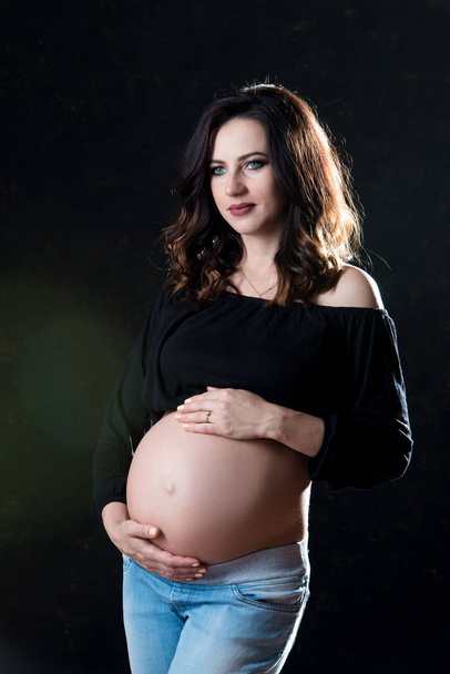 Beautiful maternity. Slim pregnant woman with hair flying in the wind on a black background. Happy pregnancy and healthy motherhood - Foto, Imagen