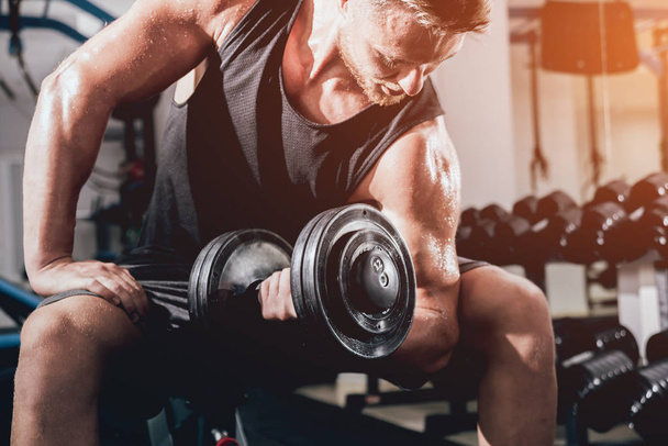 Handsome muscular man working out with dumbbells at gym - Photo, Image