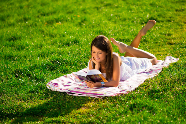 een jonge vrouw liggen op het gras en lezen van een boek - Foto, afbeelding