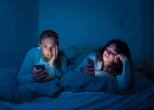 Life style portrait of young bored couple in bed at night on smart phones obsessed with games, social media, apps ignoring each other. Relationship communication problems and phone addiction concept. - Fotoğraf, Görsel
