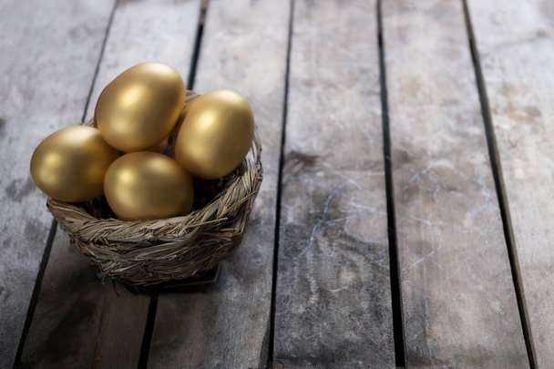Huevos dorados en nido sobre fondo oscuro de madera vintage
 - Foto, Imagen
