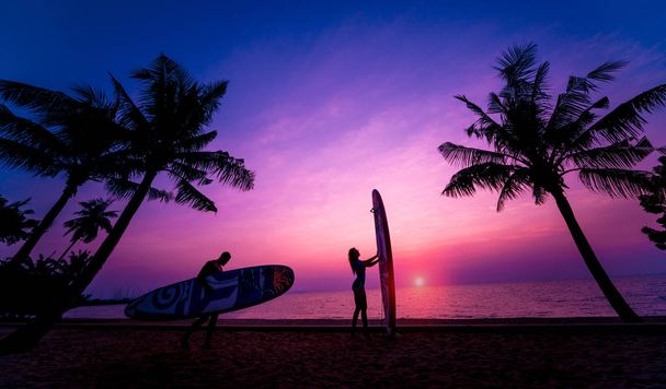 Silhouette of surfers couple holding long surf boards at sunset on tropical beach. Background - Fotografie, Obrázek