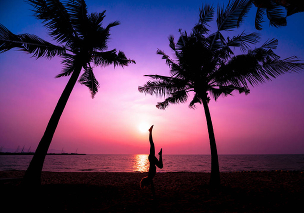 Όμορφη νεαρή γυναίκα practic γιόγκα στην παραλία. Άσκηση νωρίς το πρωί. Ανατολή του ηλίου. Παλάμες φόντο - Φωτογραφία, εικόνα